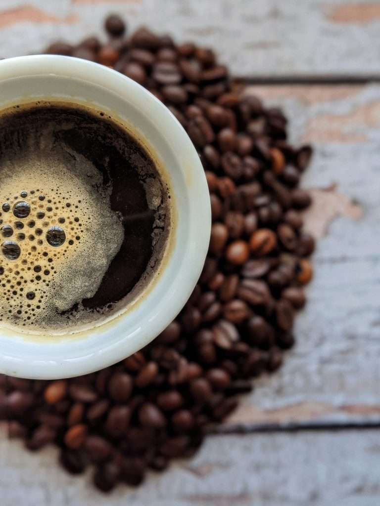 A freshly brewed cup of coffee sits among scattered beans, visually embodying its status as the champion of caffeine and chai.