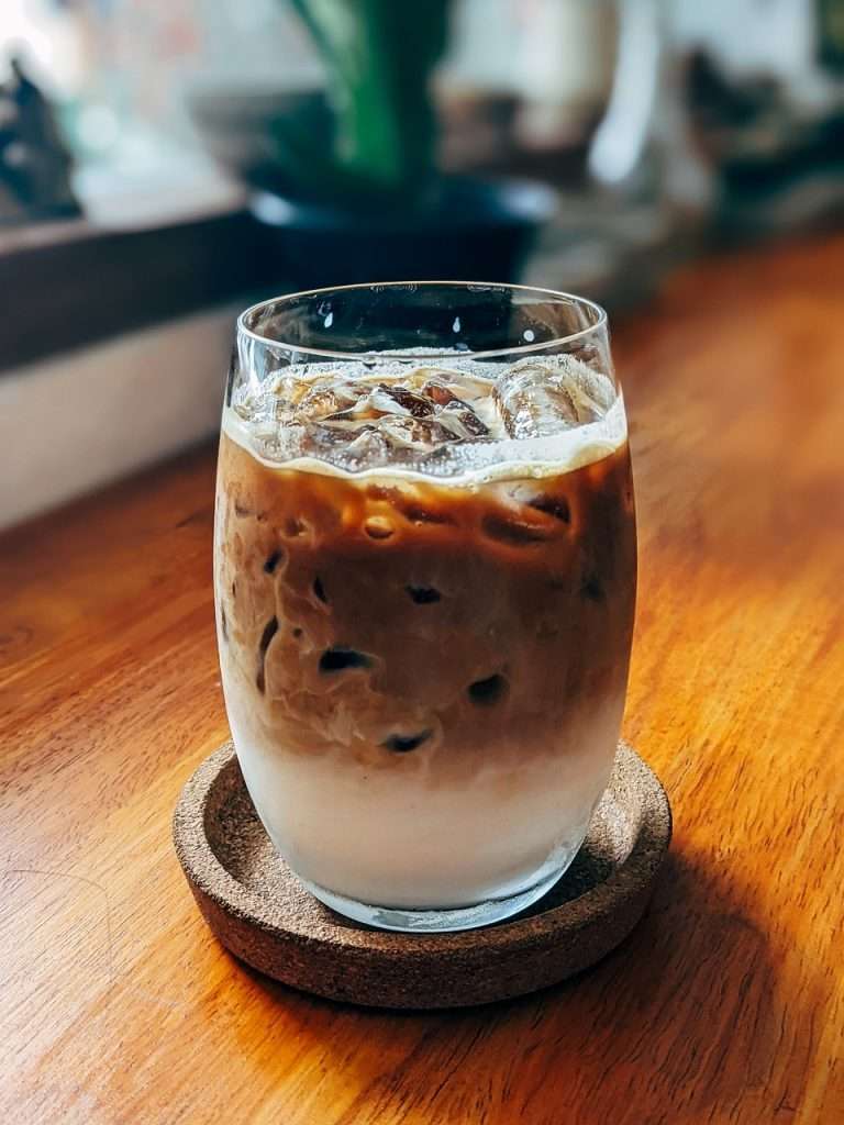 Glass of cold brew with ice on cork coasters on a wooden table.