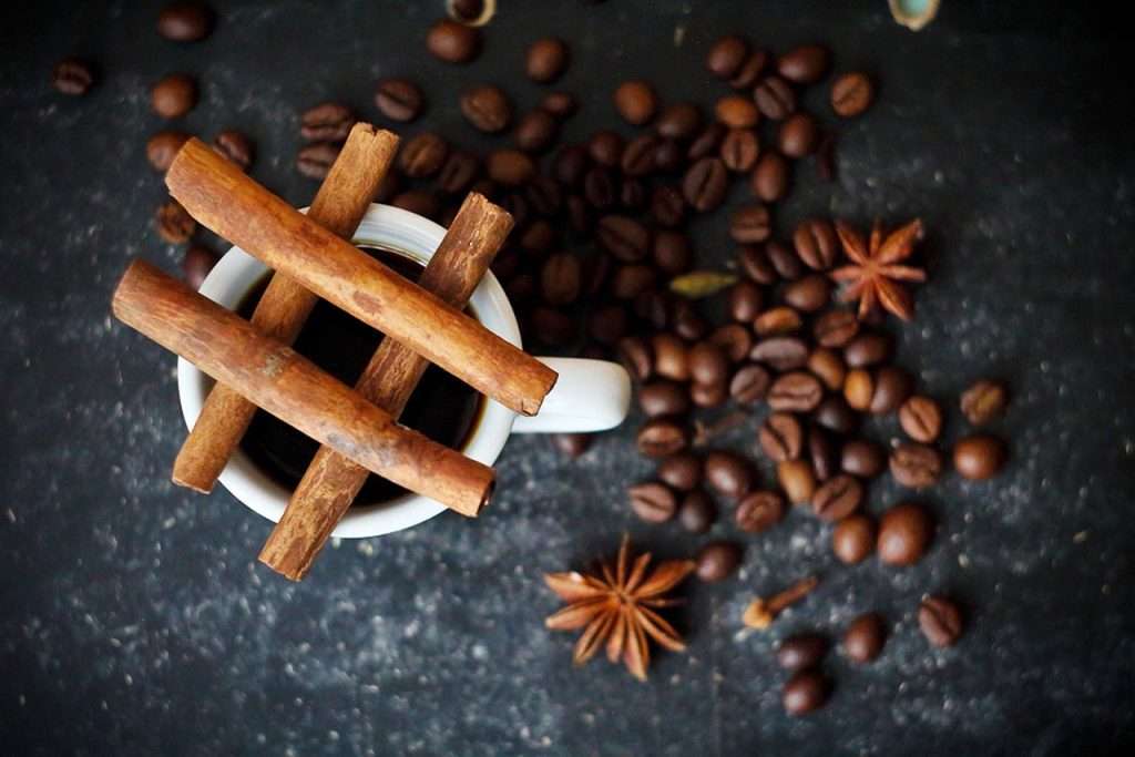 Cinnamon sticks on a cup of coffee with coffee beans and star anise around on a dark background.