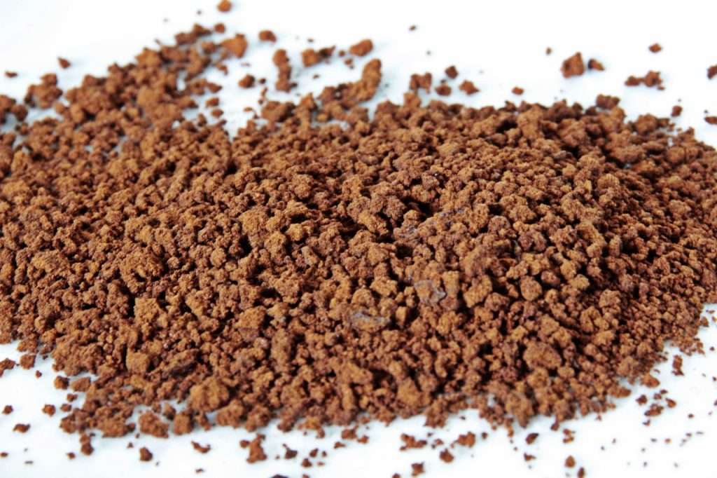 Scoop of finely ground instant coffee on white background.