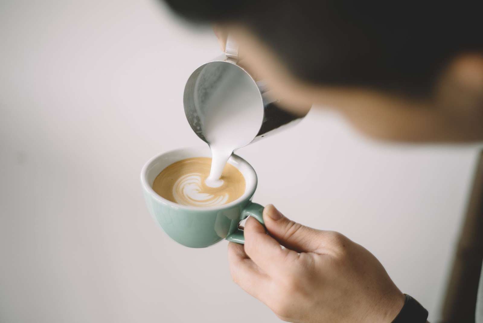 A person pouring steamed half-and-half into a cup of espresso.