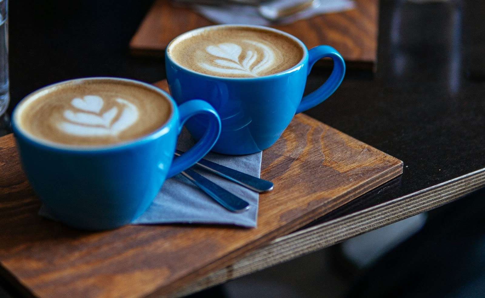  Two blue coffee cups with a heart-shaped latte art on a wooden table.