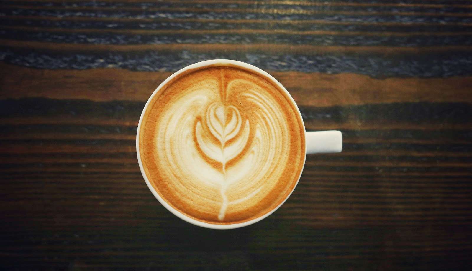 Top view of a cappuccino with intricate latte art on a wooden table.