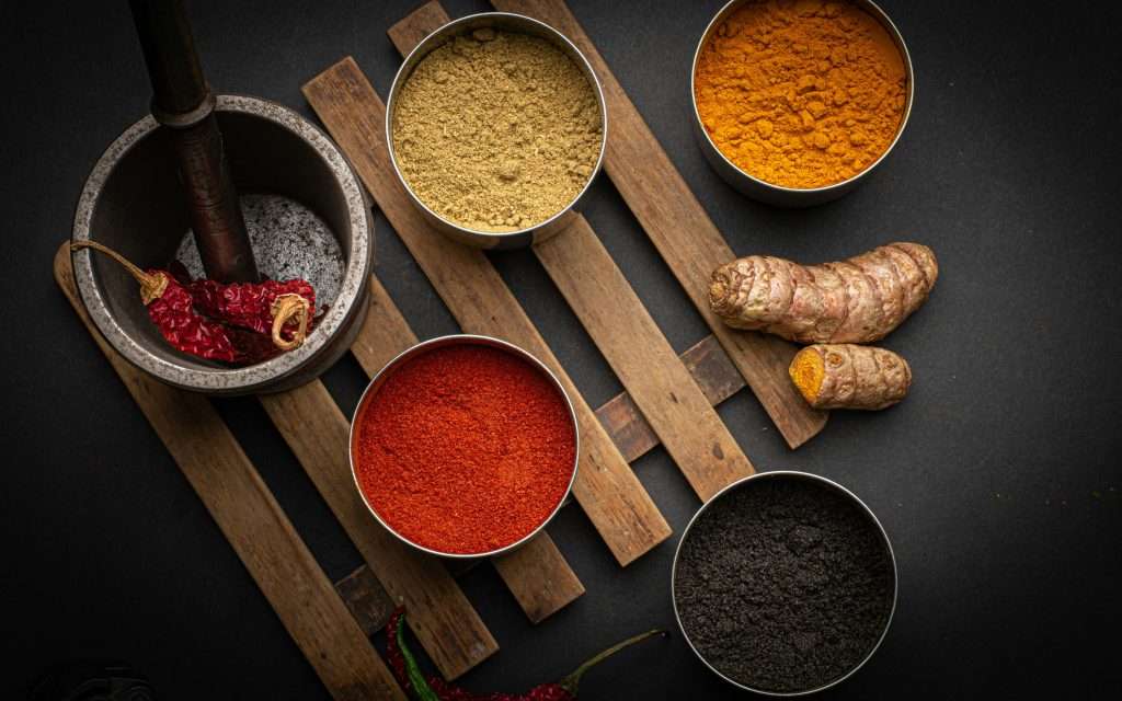 Variety of spices, including chili, turmeric and coffee powder, artistically arranged on dark background